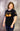 Model wearing black night shift t-shirt while looking downward toward left sleeve with Full Kode logo.